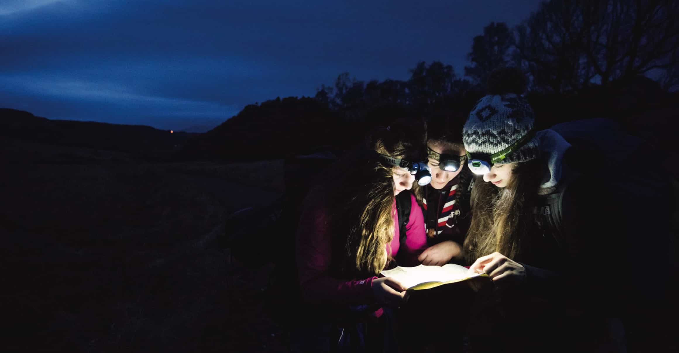 A group of 3 Female Explorers in the dark reading a map with headtorches